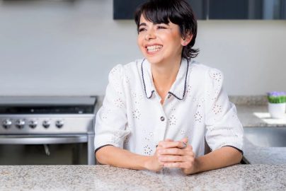 A cheerful woman leaning on a granite countertop in a modern kitchen.